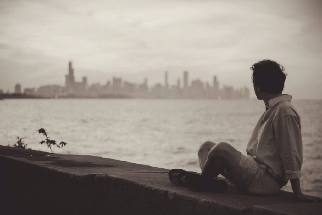 A man sitting on the beach looking out at the water.